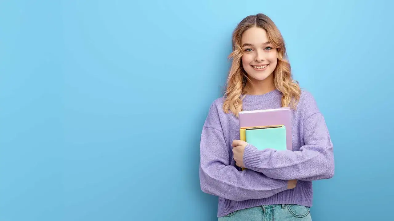 Lächelnde junge Frau mit Büchern in den Armen, bereit zum Abitur.
