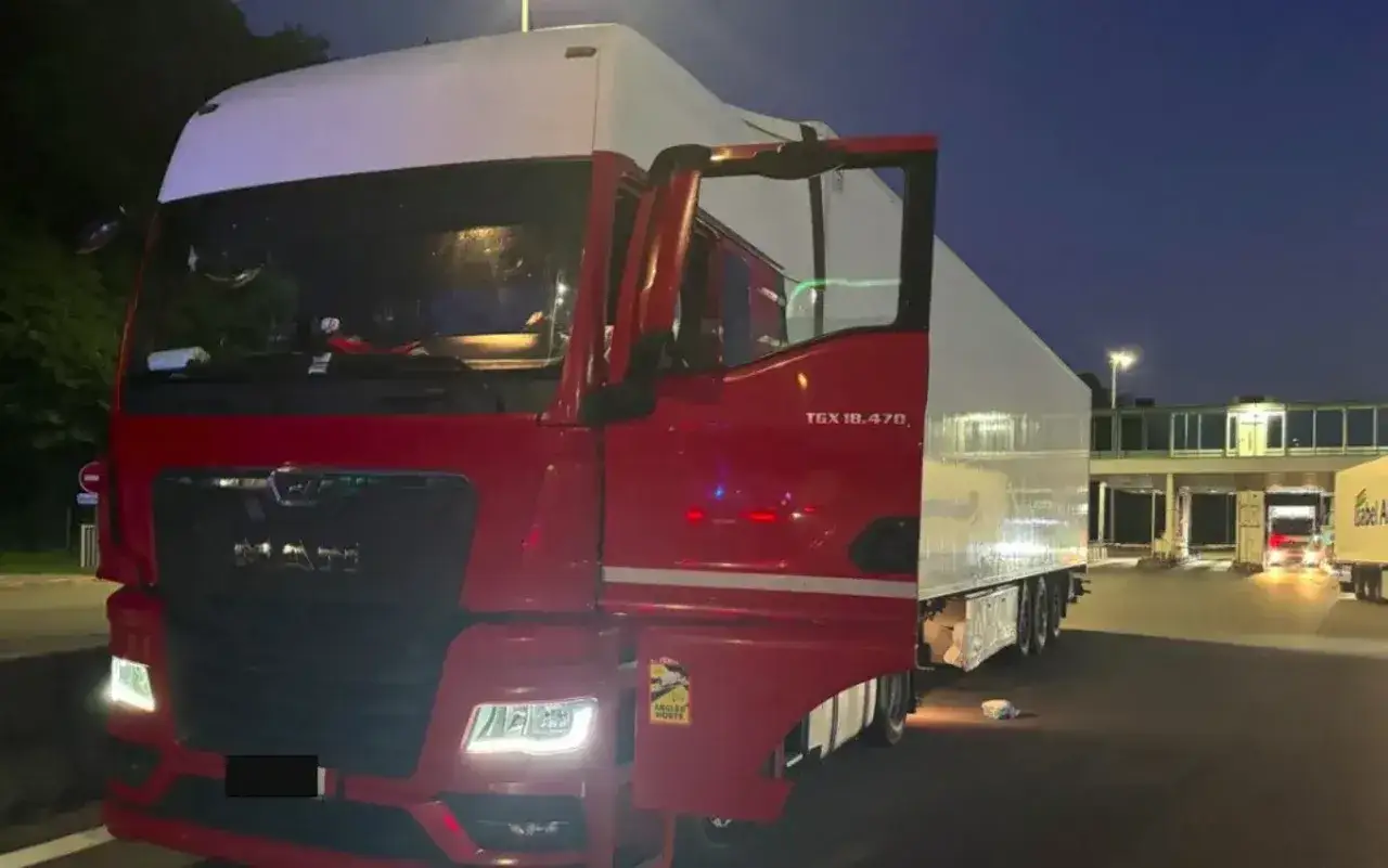 Gros plan d'un camion rouge et blanc, porte ouverte, prêt pour le chargement. Le véhicule est garé dans une zone de transit, peut-être une aire de repos ou un quai de chargement.