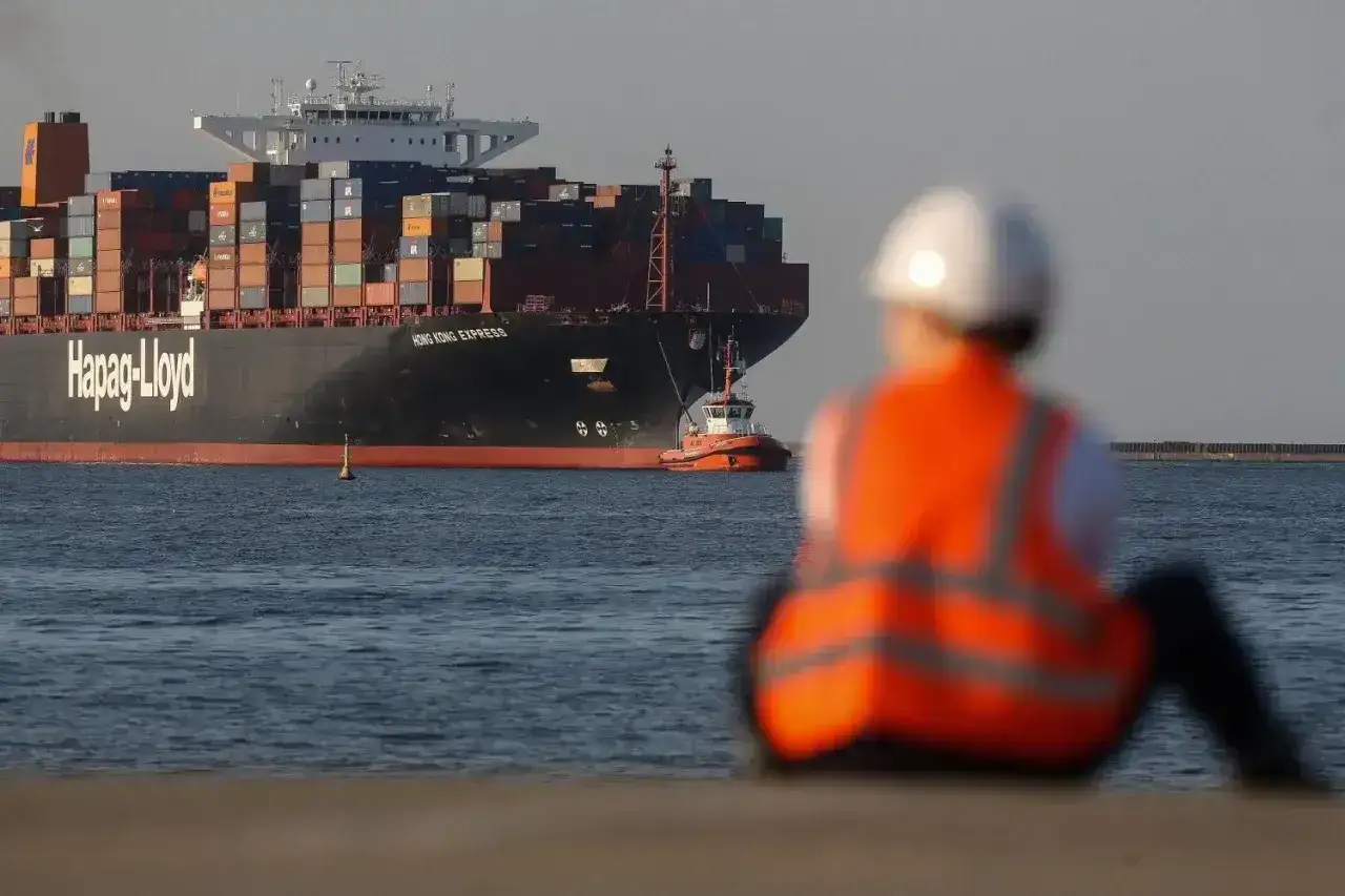 Osoba w kamizelce odblaskowej obserwuje potężny kontenerowiec Hapag-Lloyd. Zastanawiasz się, ile zarabia marynarz na kontenerowcu?