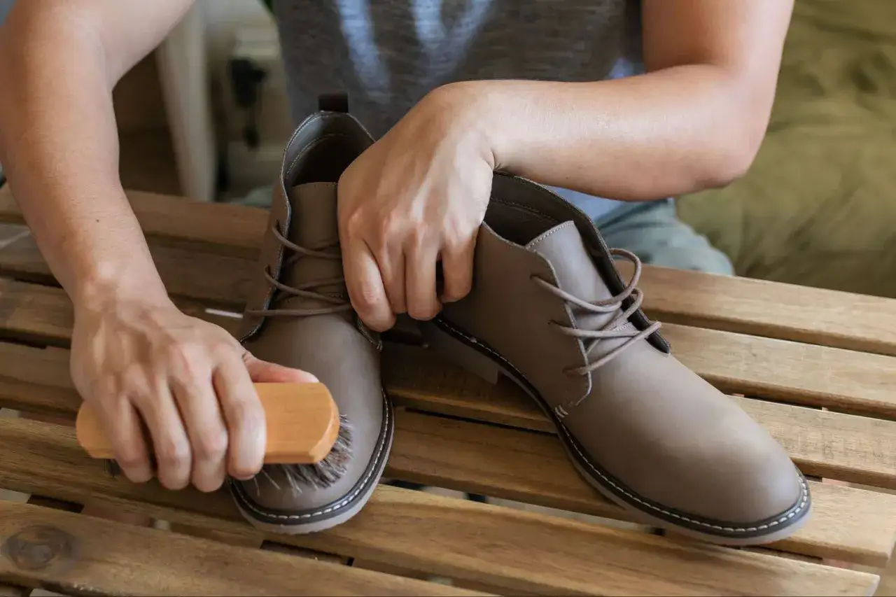Mani che spazzolano scarpe marroni su un tavolo di legno. Un modo semplice per pulire le scarpe senza lavarle.