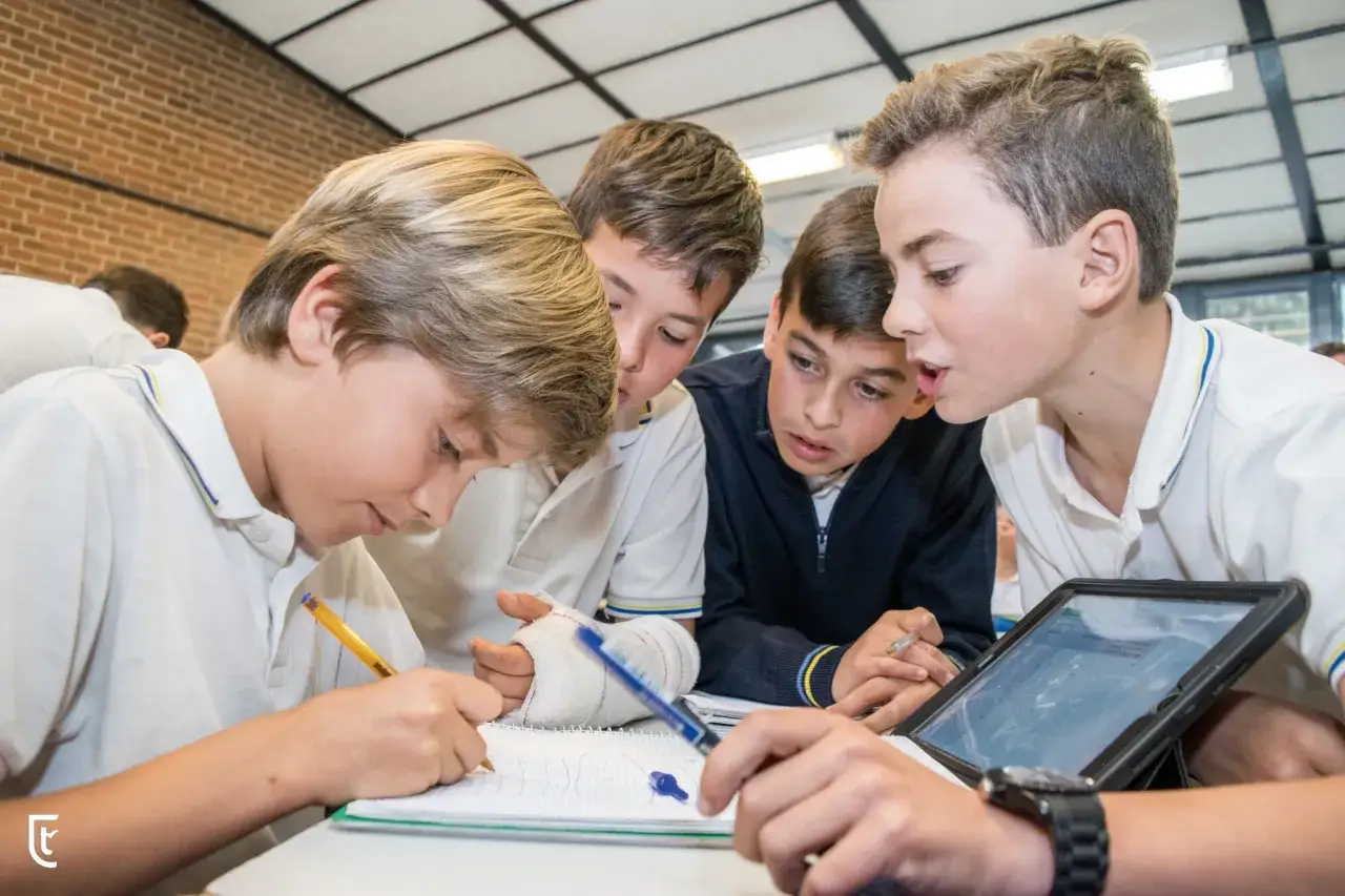 Chicos colaboran en un proyecto, mostrando la **educaci&oacute;n personalizada** con un cuaderno, tablet y un brazo vendado.