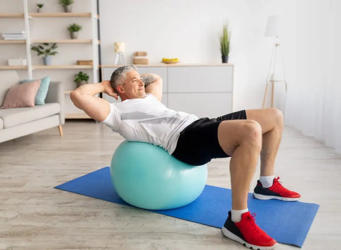 Homme faisant un exercice swiss ball pour renforcer ses abdominaux, confortablement installé chez lui.