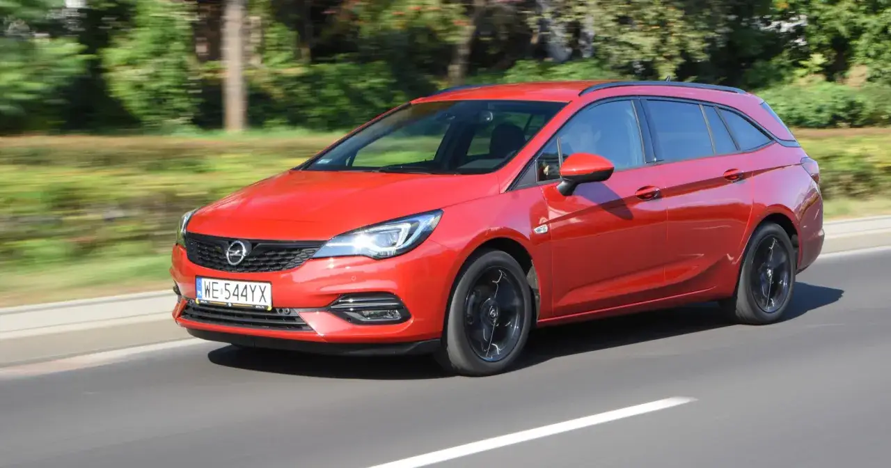 Czerwona Opel Astra Turbo kombi w ruchu, z widocznym kierowcą.