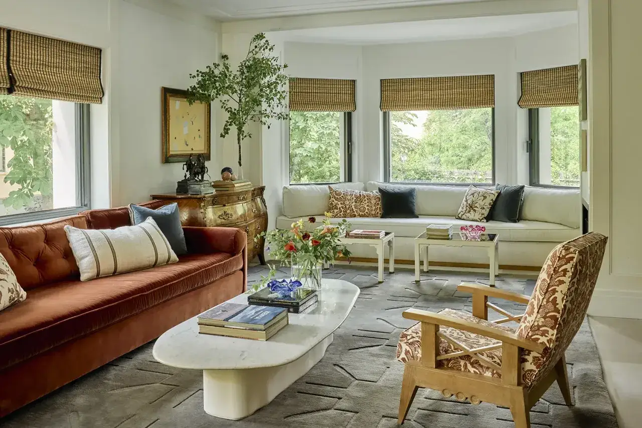 Un sal&oacute;n elegante con sof&aacute;s, mesa de centro de m&aacute;rmol y una silla de dise&ntilde;o, obra de **decoradores de interiores** que combinan texturas y colores.