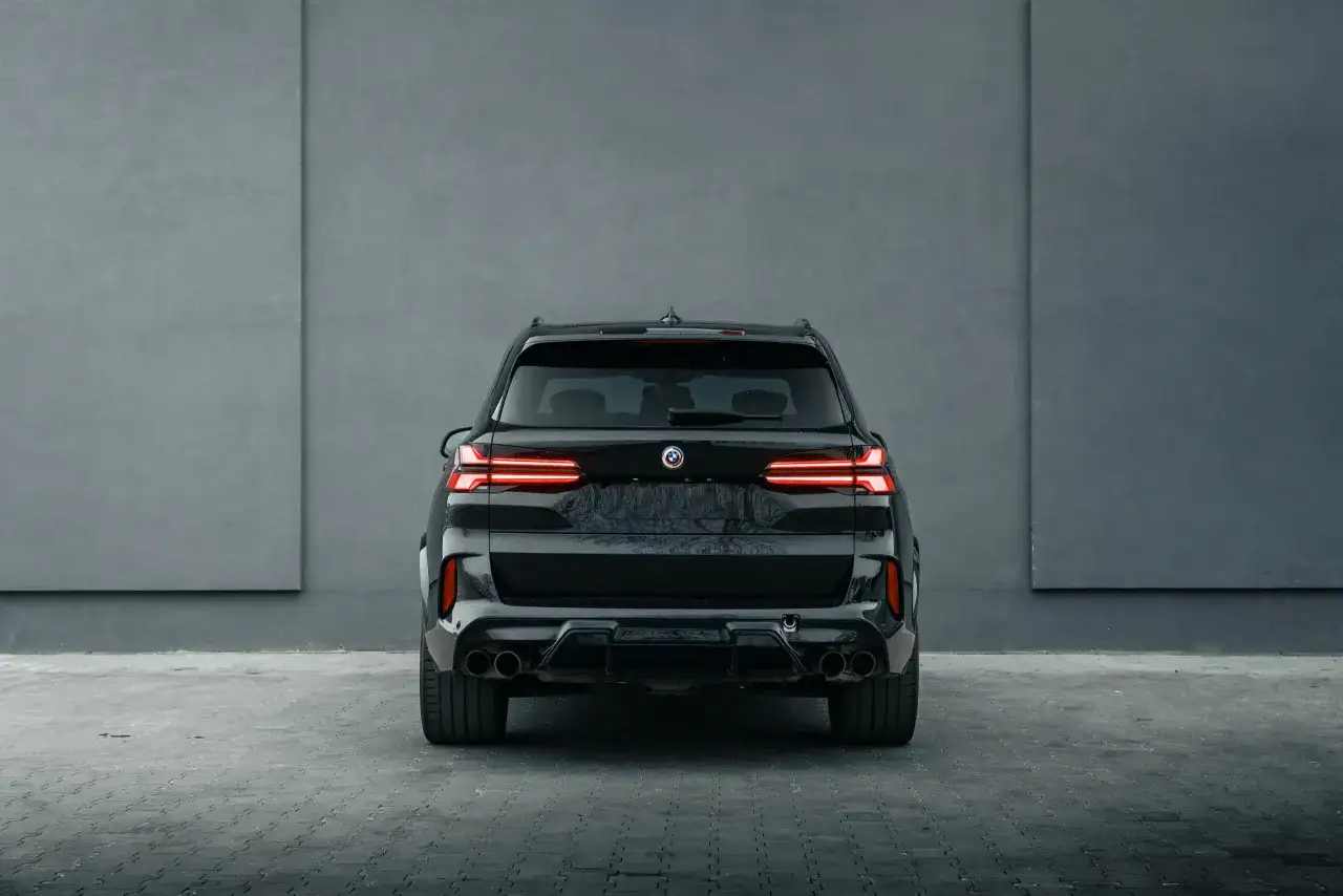 Czarny SUV klasy premium z charakterystycznymi światłami LED i podwójnymi końcówkami wydechu, zaparkowany przed betonową ścianą.