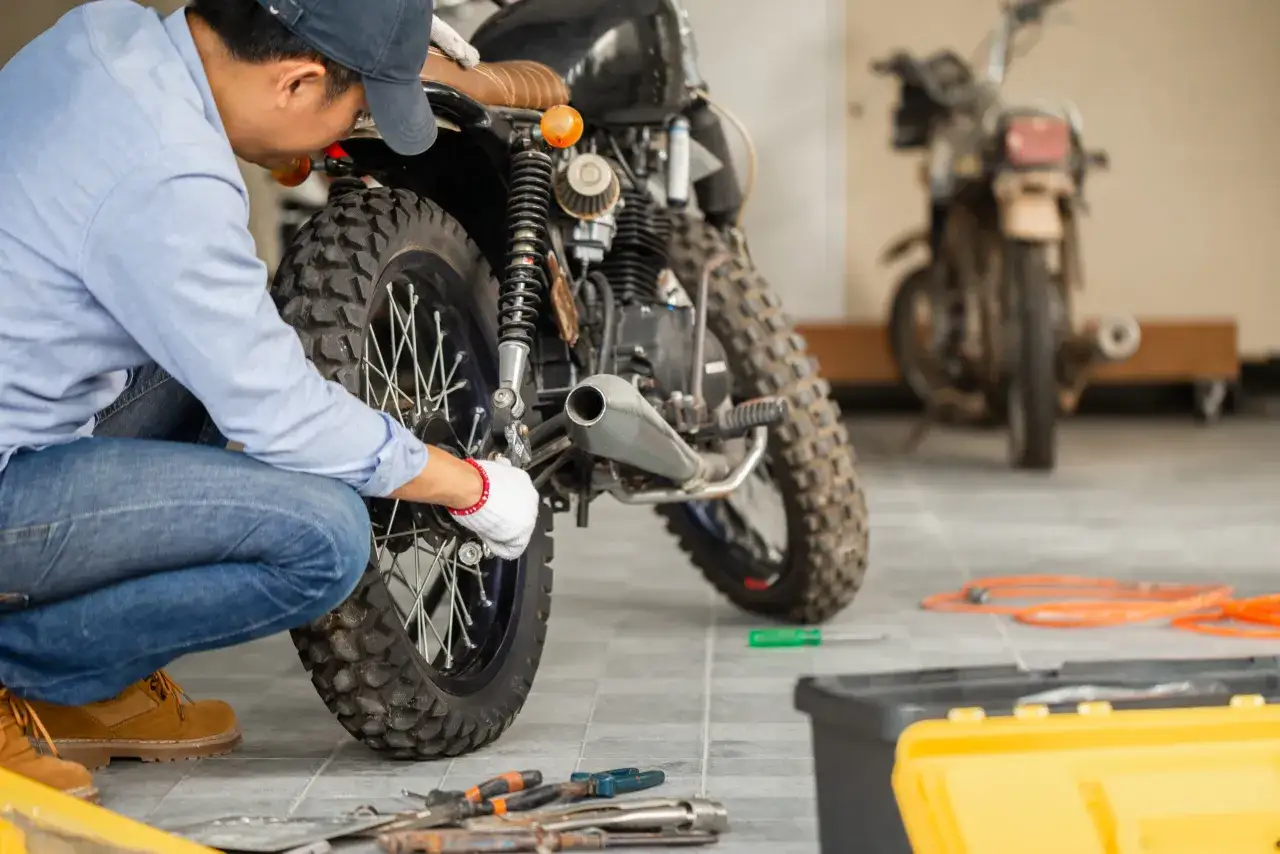Mec&aacute;nico revisa moto custom para pasar la primera ITV. Herramientas y otra moto al fondo.