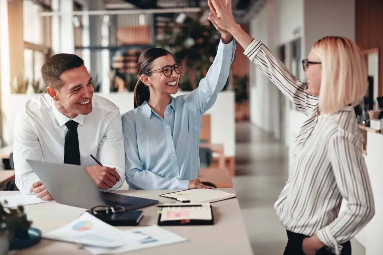 Trois collègues célèbrent un succès. La reconnaissance au travail est palpable dans leurs sourires et leur high five.