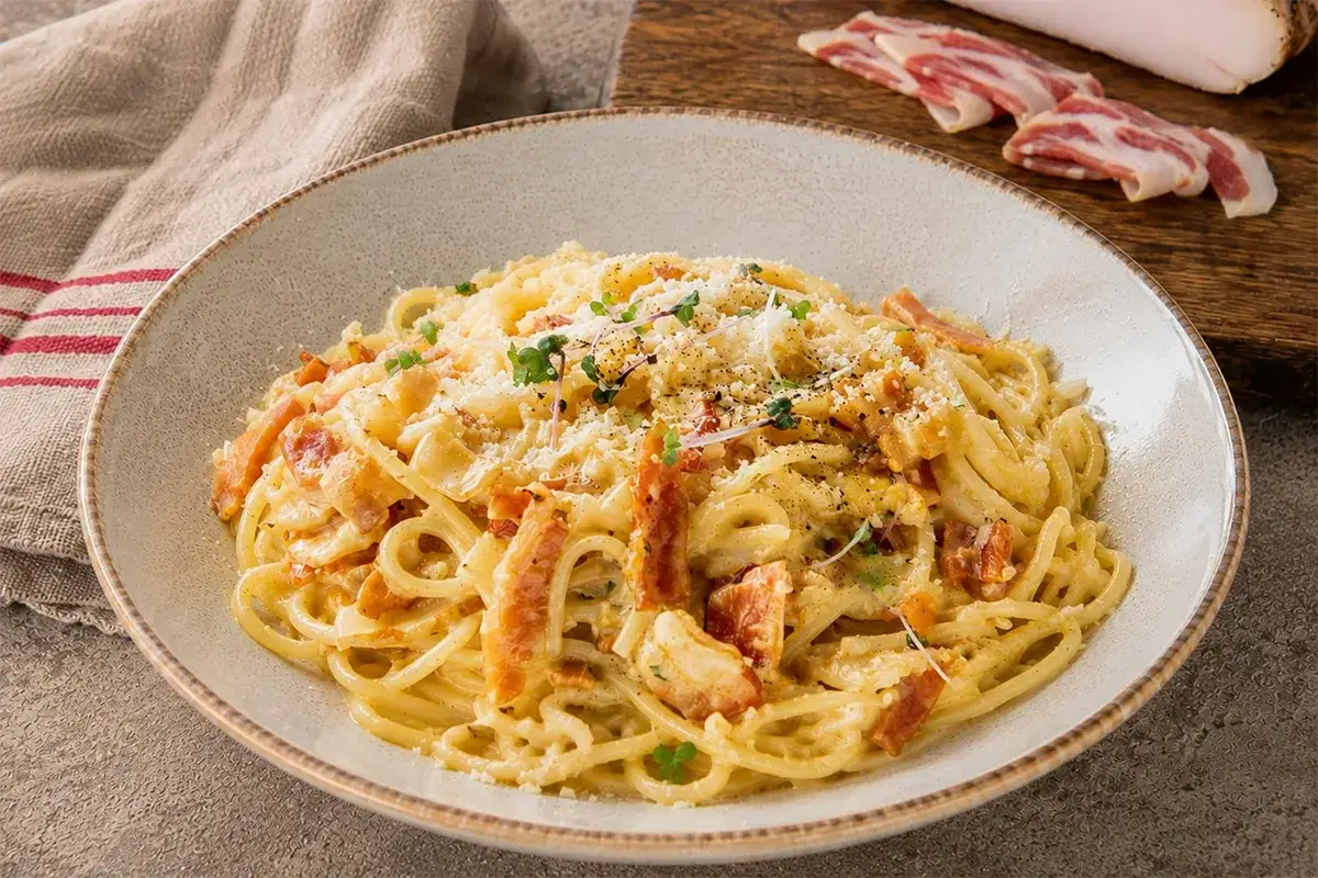 Un plat de spaghetti crémeux, garni de guanciale croustillant et de parmesan râpé, évoquant la vraie recette carbonara italienne.