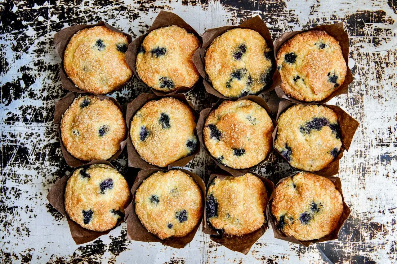 Zwölf goldbraune Blaubeermuffins mit knuspriger Kruste und saftigen Blaubeeren, bereit für ein köstliches Blaubeermuffins Rezept.