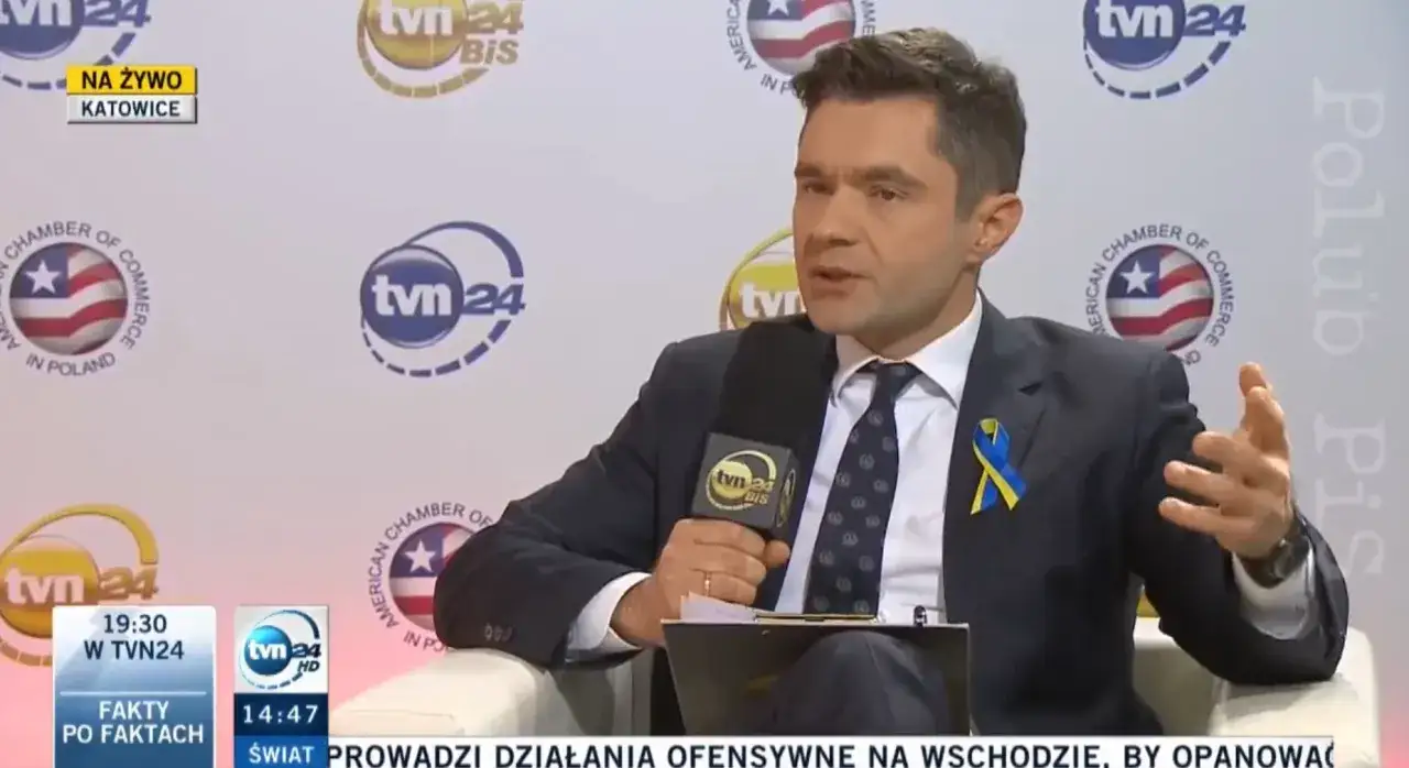 Jan Niedziałek, dziennikarz w garniturze z niebiesko-żółtą wstążką, udziela wywiadu w studio TVN24.