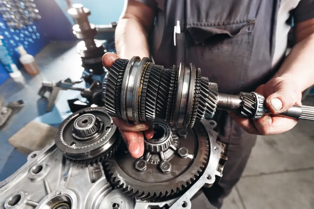 Mechanik pokazuje wałek z zębatkami skrzyni biegów. Rozważasz automat czy manual? Wady i zalety obu rozwiązań są kluczowe.