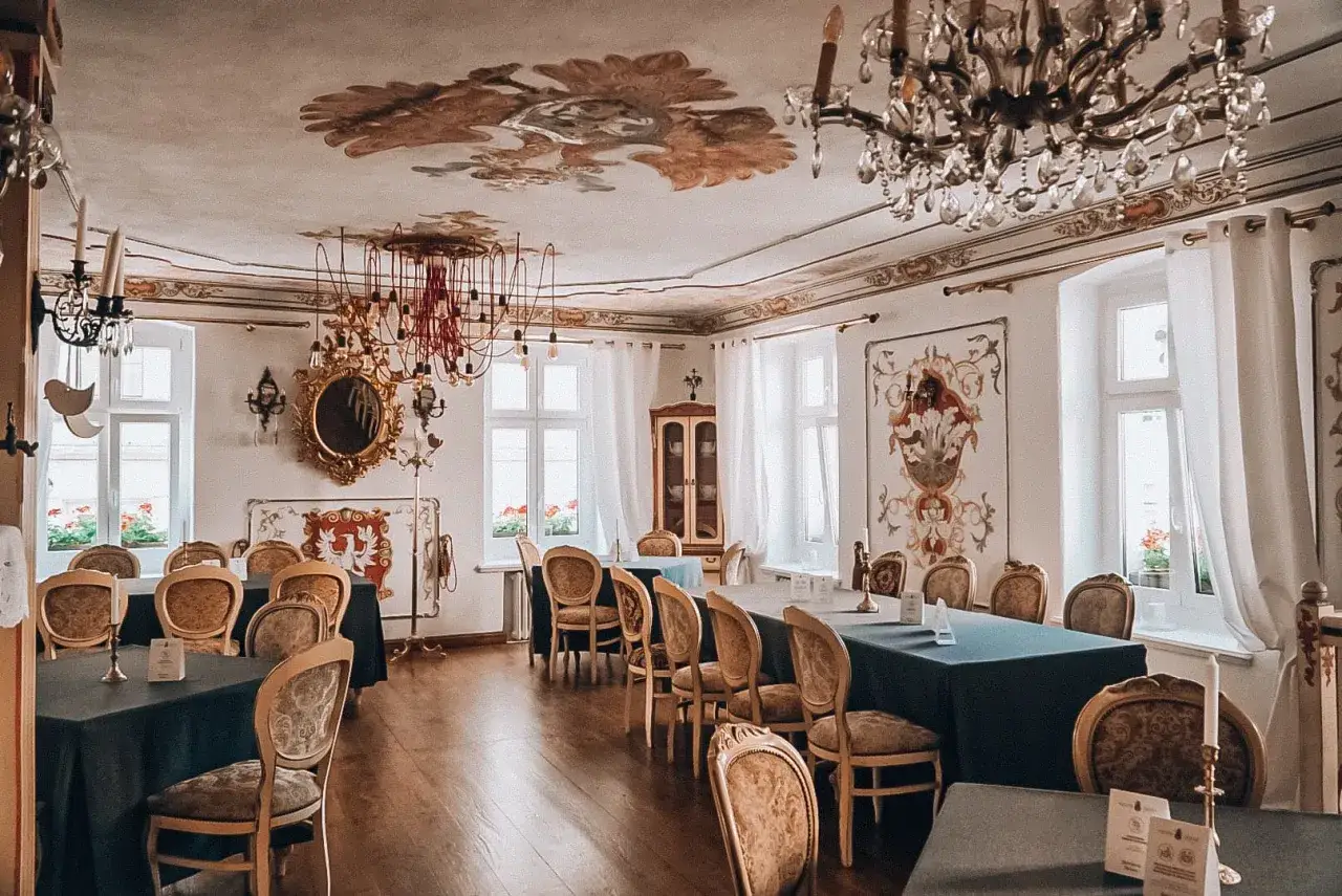 Elegancka sala bankietowa w austerii, z bogato zdobionym sufitem, kryształowymi żyrandolami i zabytkowymi meblami.