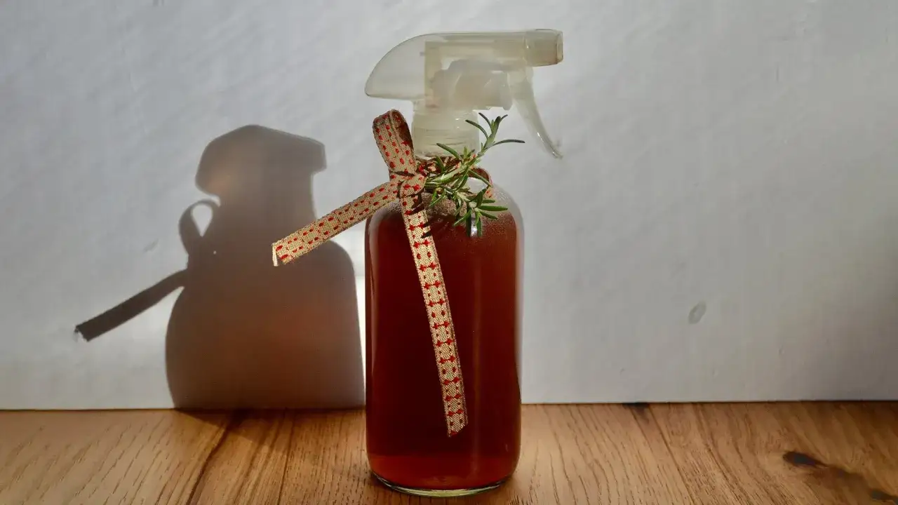 Botella con atomizador decorada con cinta y romero. El l&iacute;quido &aacute;mbar sugiere agua de romero para el pelo, un remedio natural.