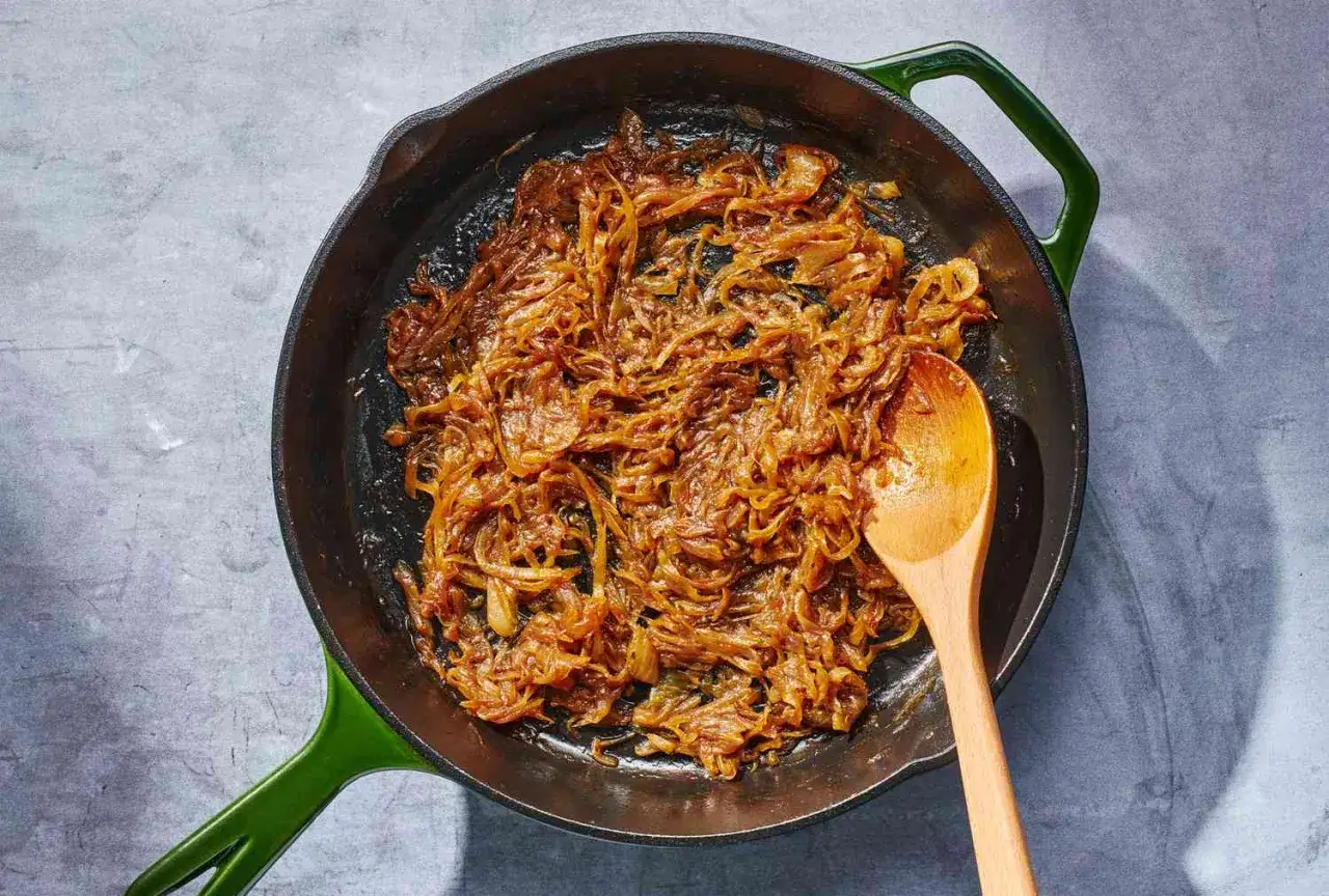 Cebolla caramelizada dorada y tierna en sartén de hierro fundido, lista para añadir sabor a cualquier plato.