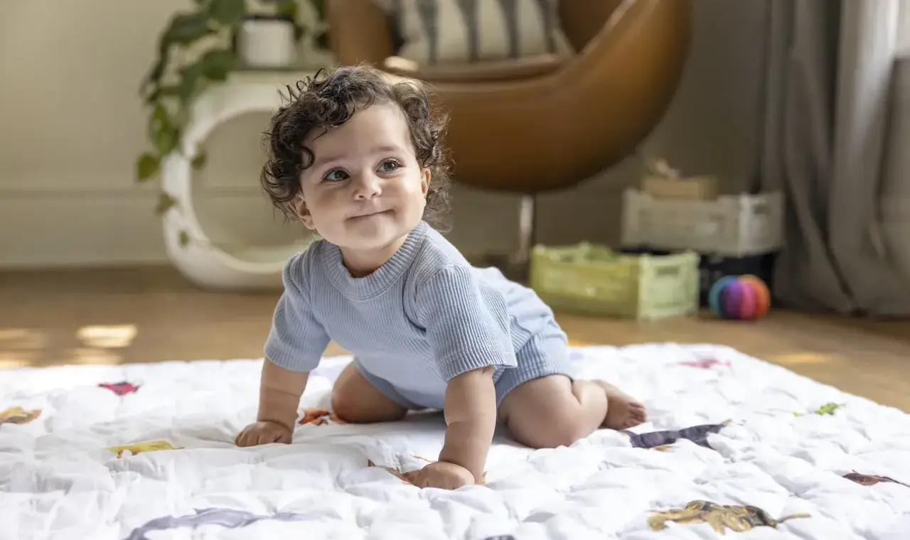 Ein Baby in einem blauen Strampler übt, wie krabbeln Babys, auf einer Decke mit Tiermotiven.