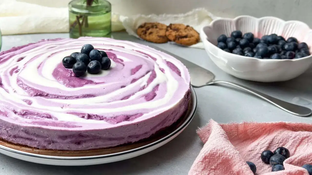 Ein k&ouml;stlicher no bake blueberry cheesecake mit einem Swirl-Muster aus Blaubeeren und Sahne, garniert mit frischen Blaubeeren.