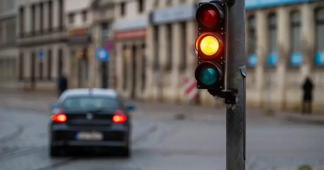 Sygnalizacja świetlna pokazuje żółte światło, a czarny samochód wykonuje przejazd na żółtym świetle.