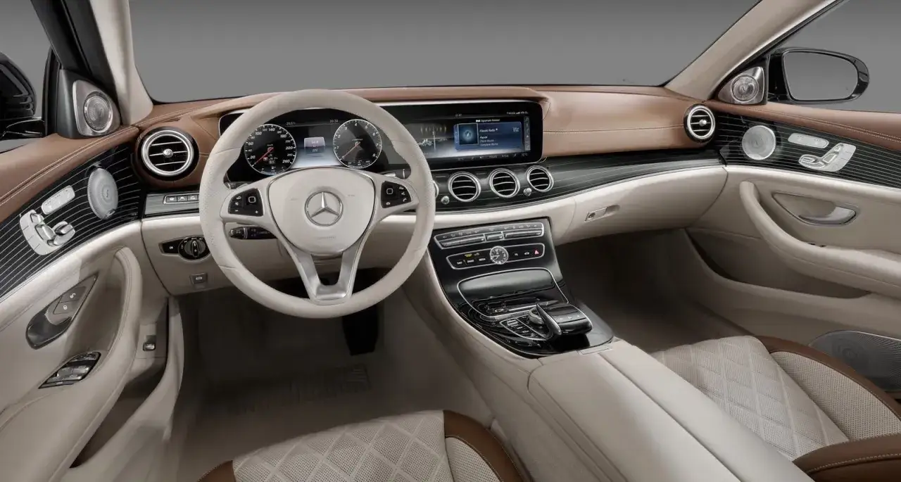 Wnętrze luksusowego Mercedesa E350 z beżową i brązową tapicerką, nowoczesnym kokpitem i ekranem multimedialnym.