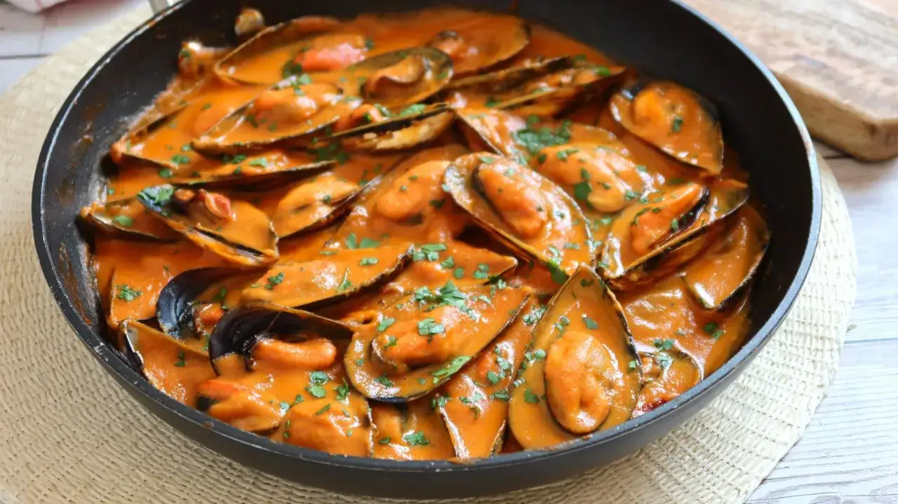 Mejillones con tomate en una sartén, cubiertos con una salsa cremosa y espolvoreados con perejil picado. ¡Un plato delicioso!