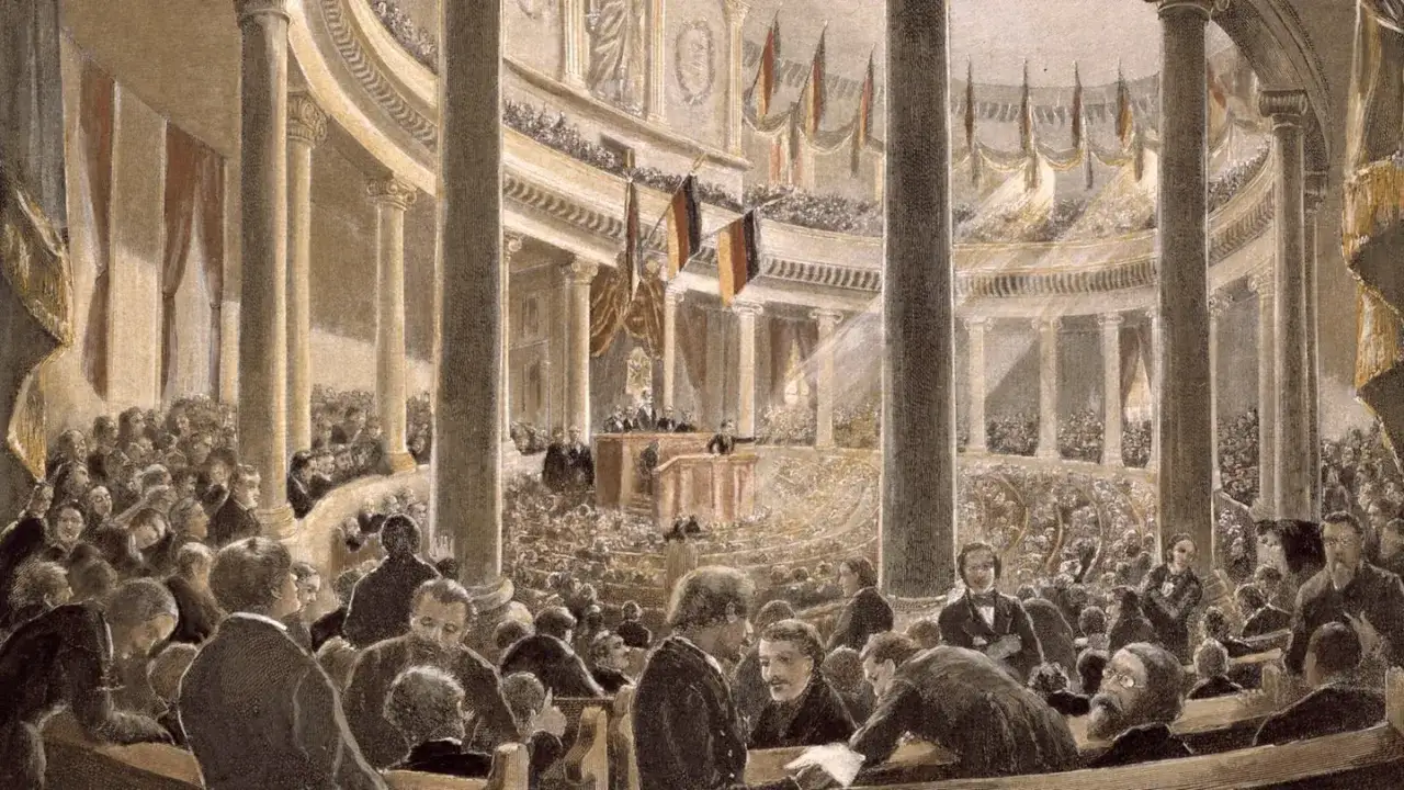 Die Frankfurter Nationalversammlung tagt in einem prunkvollen Saal. Viele Abgeordnete verfolgen gespannt die Debatte.