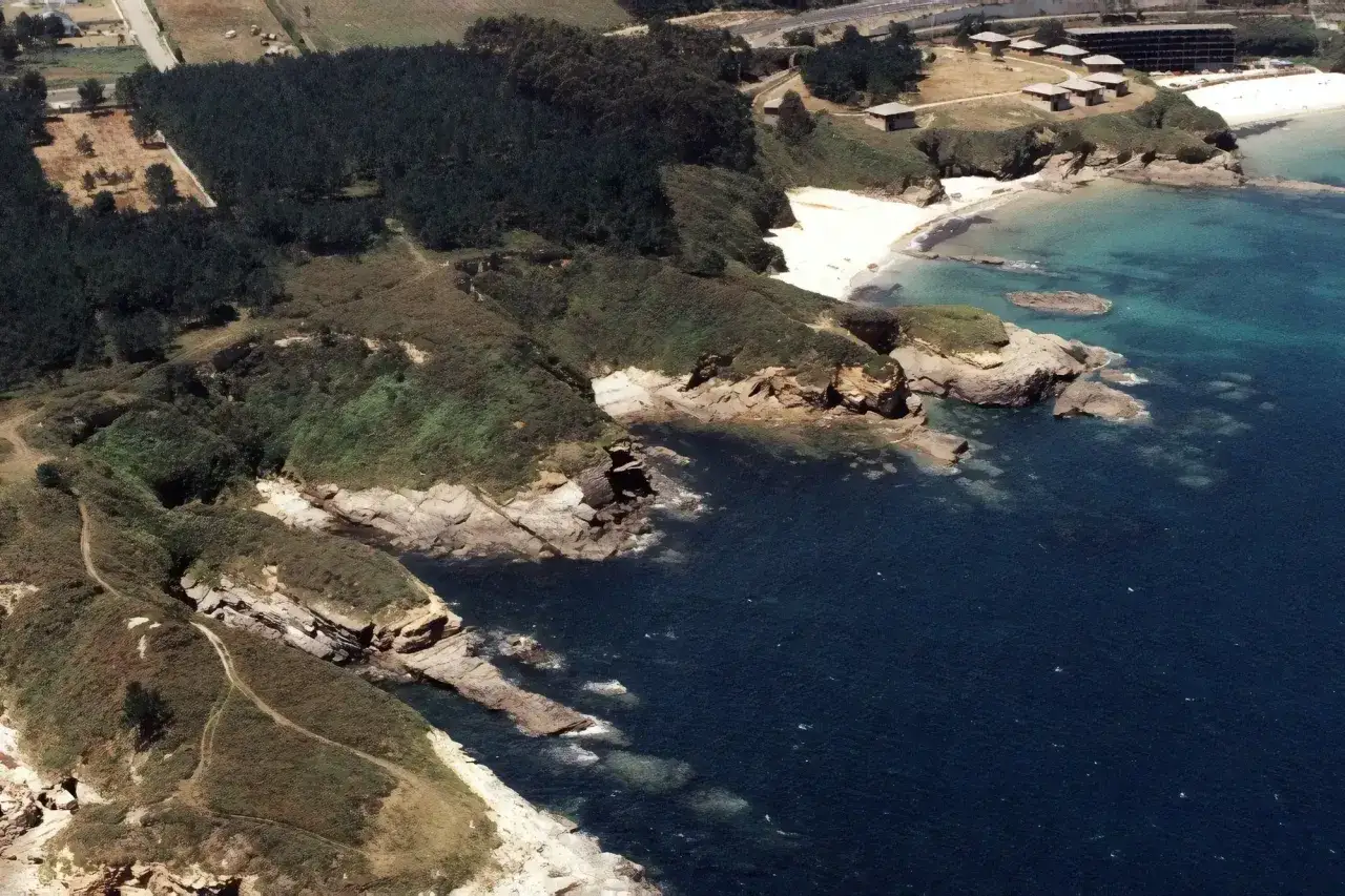 Vista aérea de la playa de los alemanes en Foz, con acantilados rocosos, vegetación y el mar azul.
