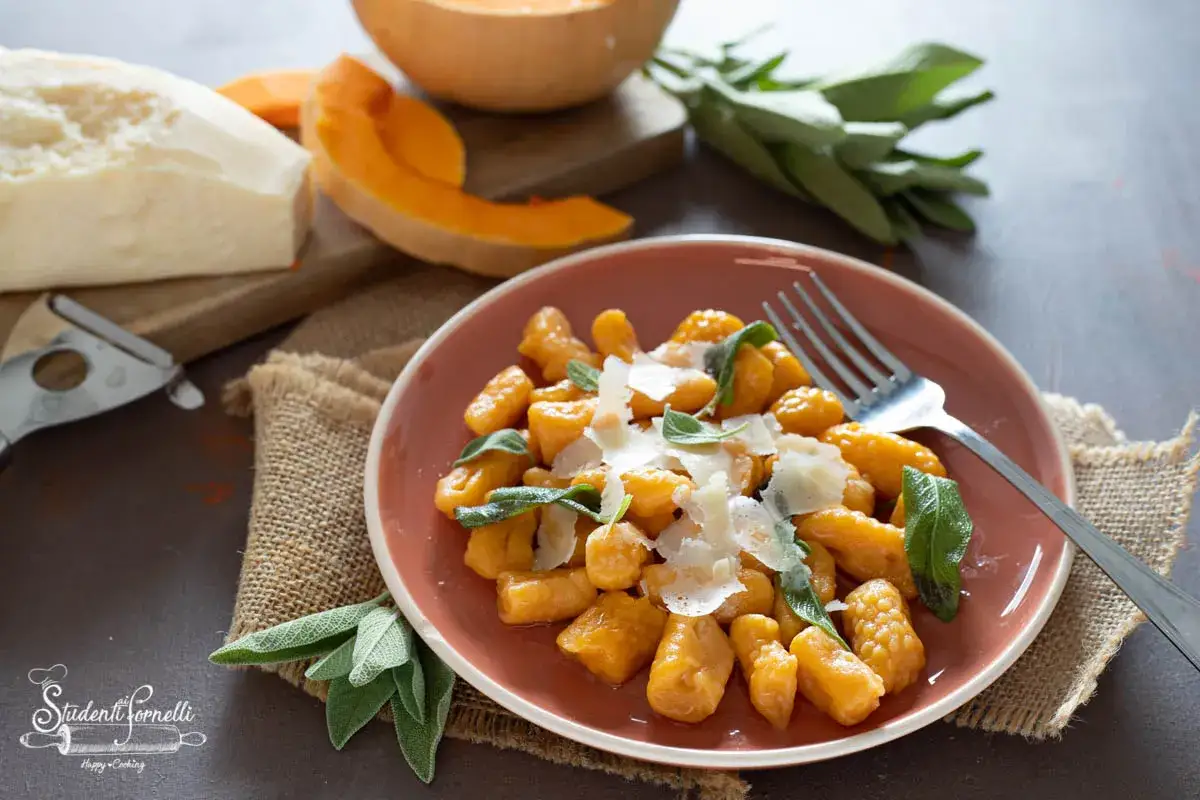 Gnocchi di zucca dorati, guarniti con parmigiano grattugiato e foglie di salvia fresca, pronti per essere gustati.