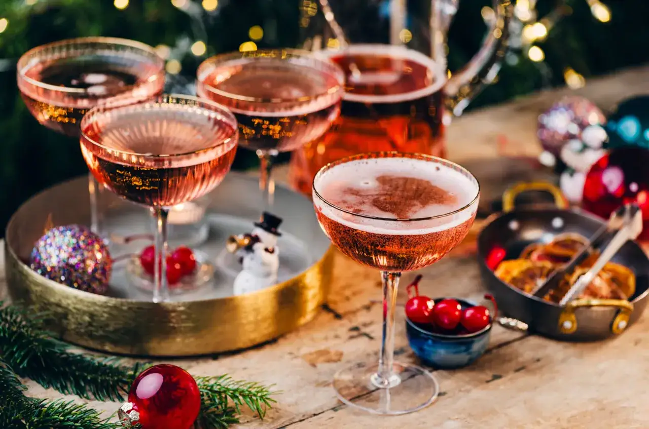 Różowy drink z szampanem, udekorowany wiśniami i świątecznymi ozdobami, zaprasza do celebracji.