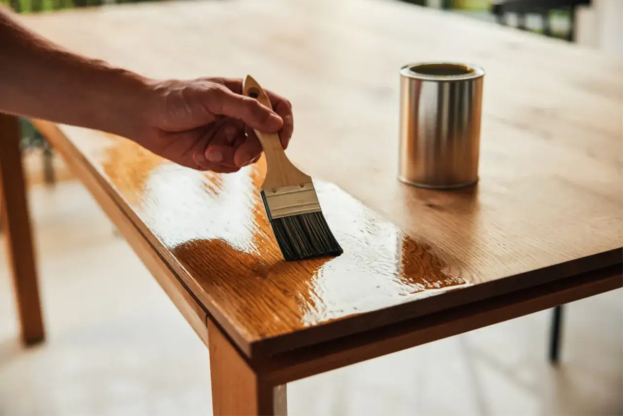 Application d'un vernis après peinture sur une table en bois. La finition brillante protège et sublime le grain du bois.
