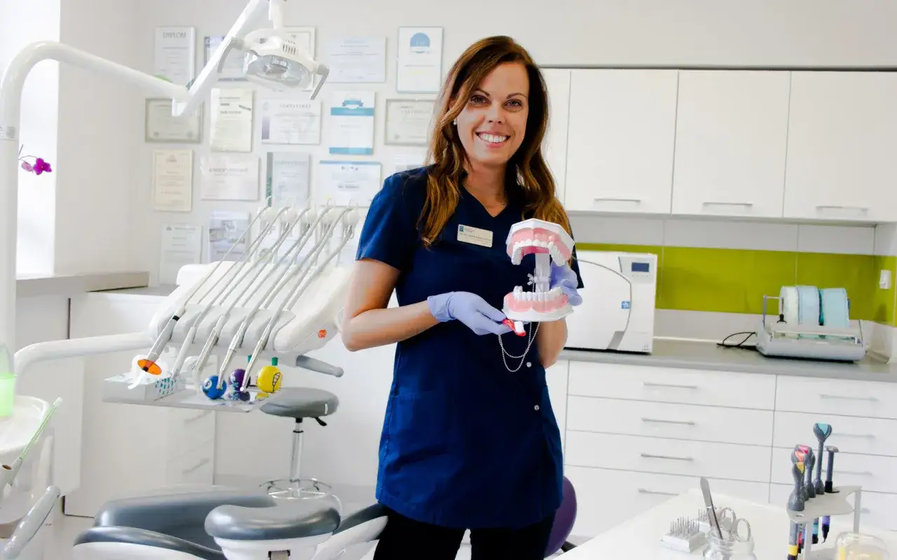 Uśmiechnięta dentystka w gabinecie trzyma model szczęki.