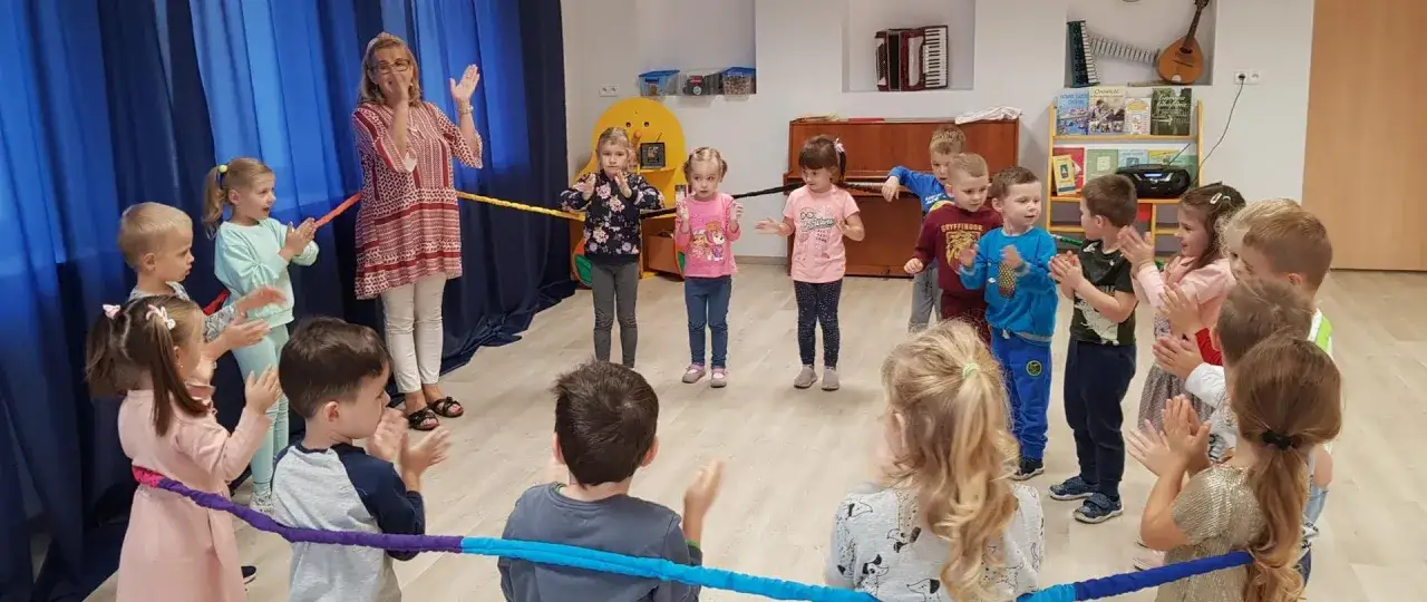 Dzieci i nauczycielka bawią się w rytm muzyki, pokazując, jak ważny jest wpływ muzyki na rozw&oacute;j dziecka.