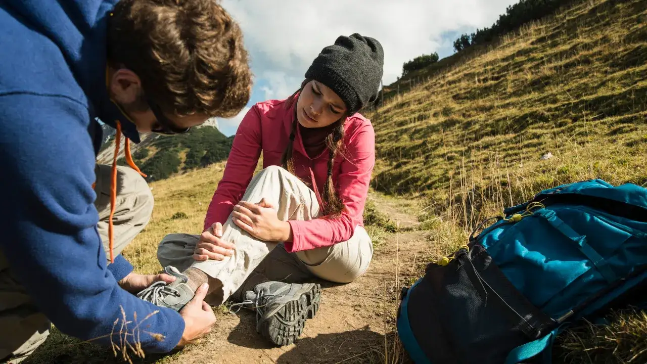 Randonneur aidant une femme souffrant d'une entorse au pied sur un sentier de montagne.