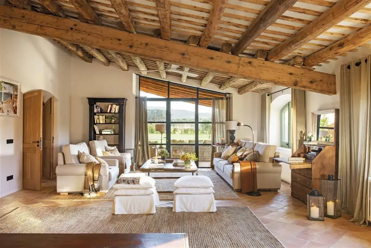 Acogedor salón con vigas de madera y vistas al campo. Ideas para casas de campo: sofás cómodos, chimenea rústica y luz natural.