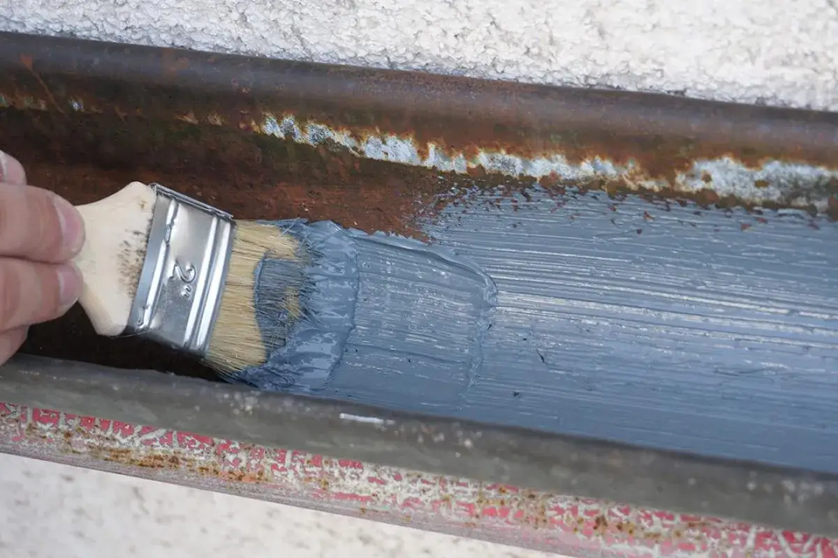 Pinsel trägt graue Farbe auf verrostete Dachrinne auf, um sie abzudichten.