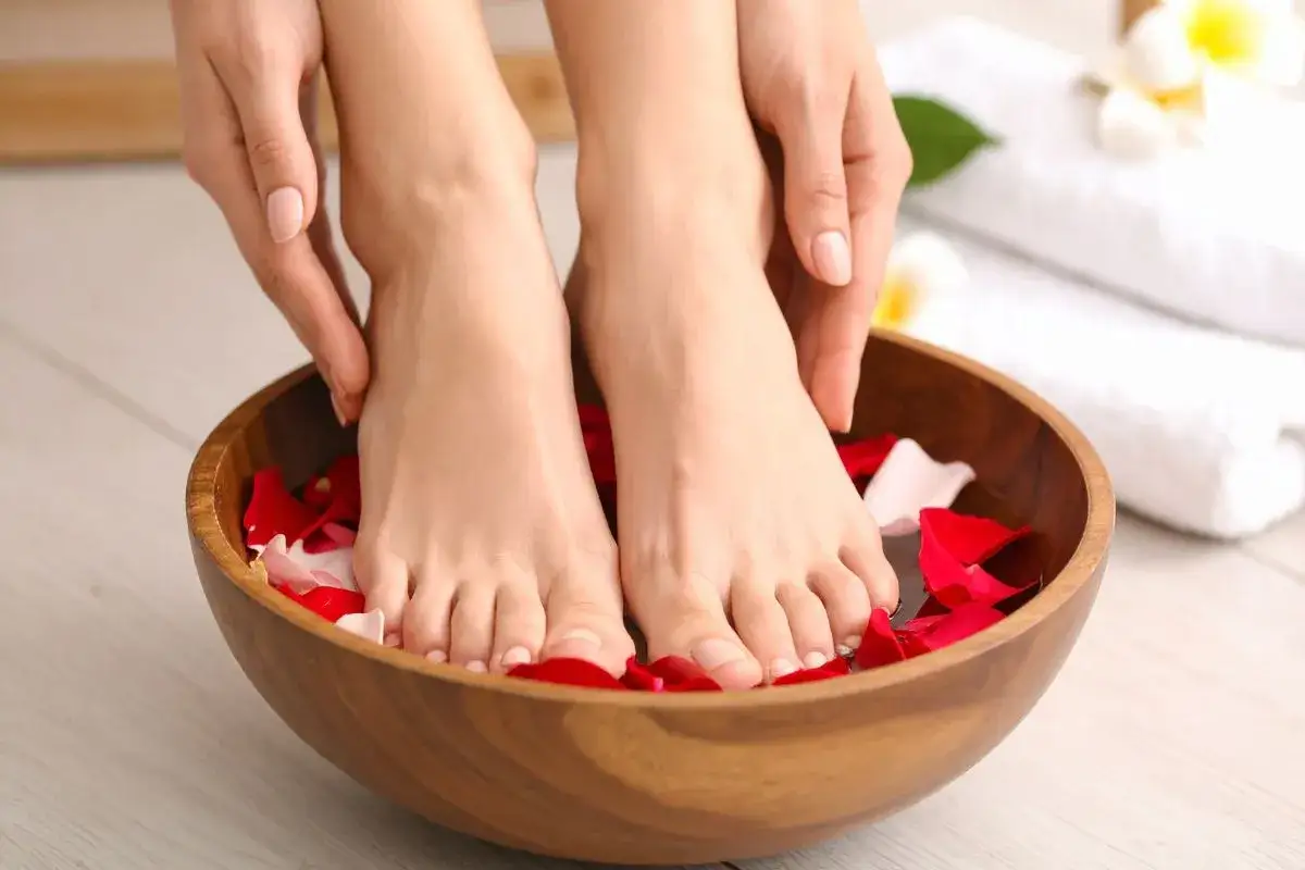 Relaksacyjny pedicure paznokcie u nóg w drewnianej misie z płatkami róż. Dłonie delikatnie dotykają stóp.