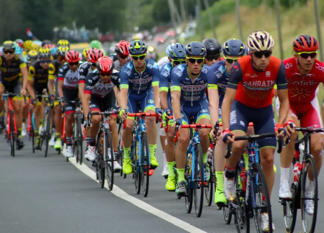 Eine Gruppe von Radfahrern, die an einer **Tour de France** teilnehmen. Man sieht viele Fahrer in voller Fahrt, die um die Führung kämpfen.