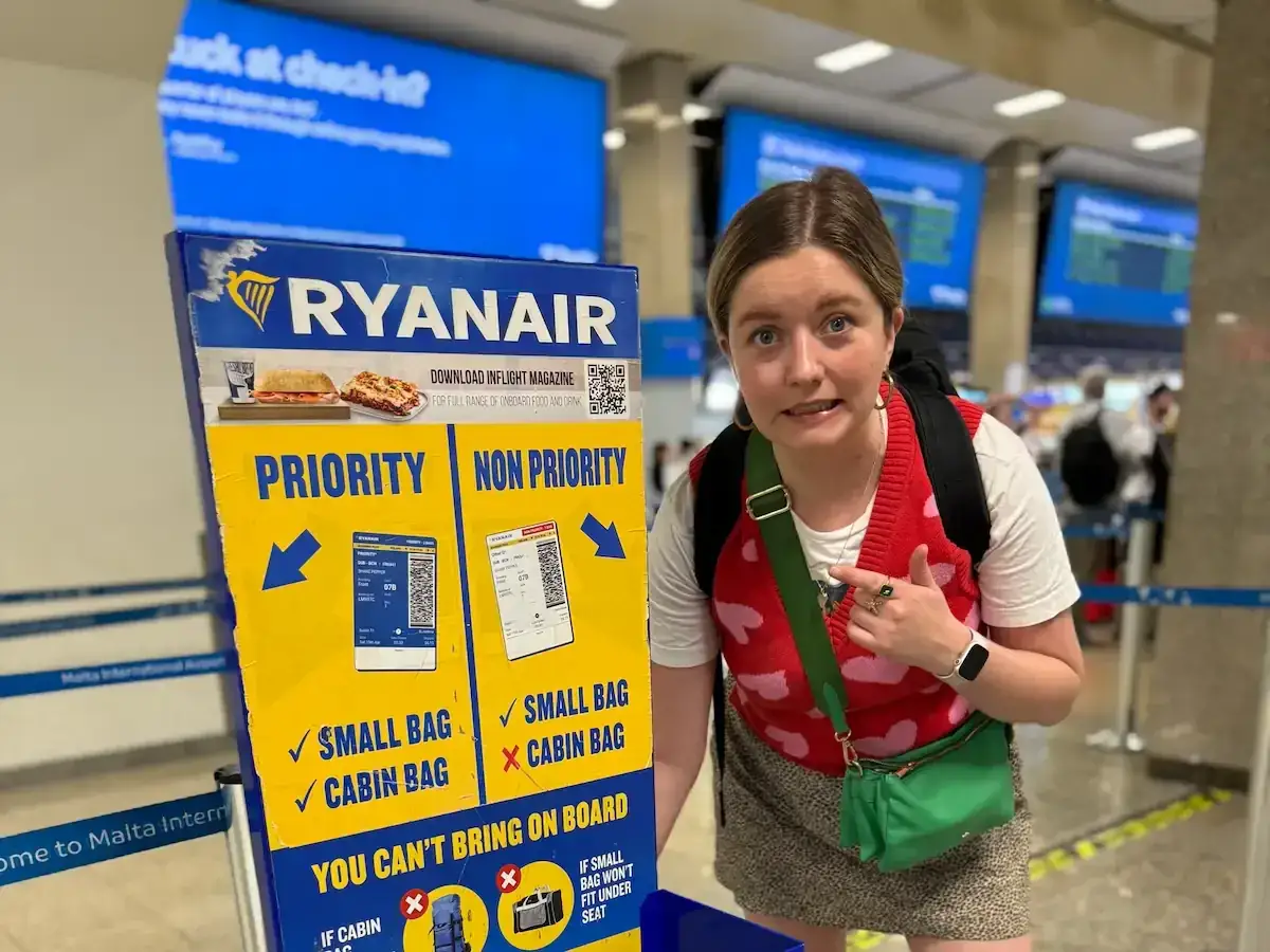 Znak Ryanair informuje, czy można wziąć jedzenie do samolotu. Kobieta z zaciekawieniem przygląda się zasadom.