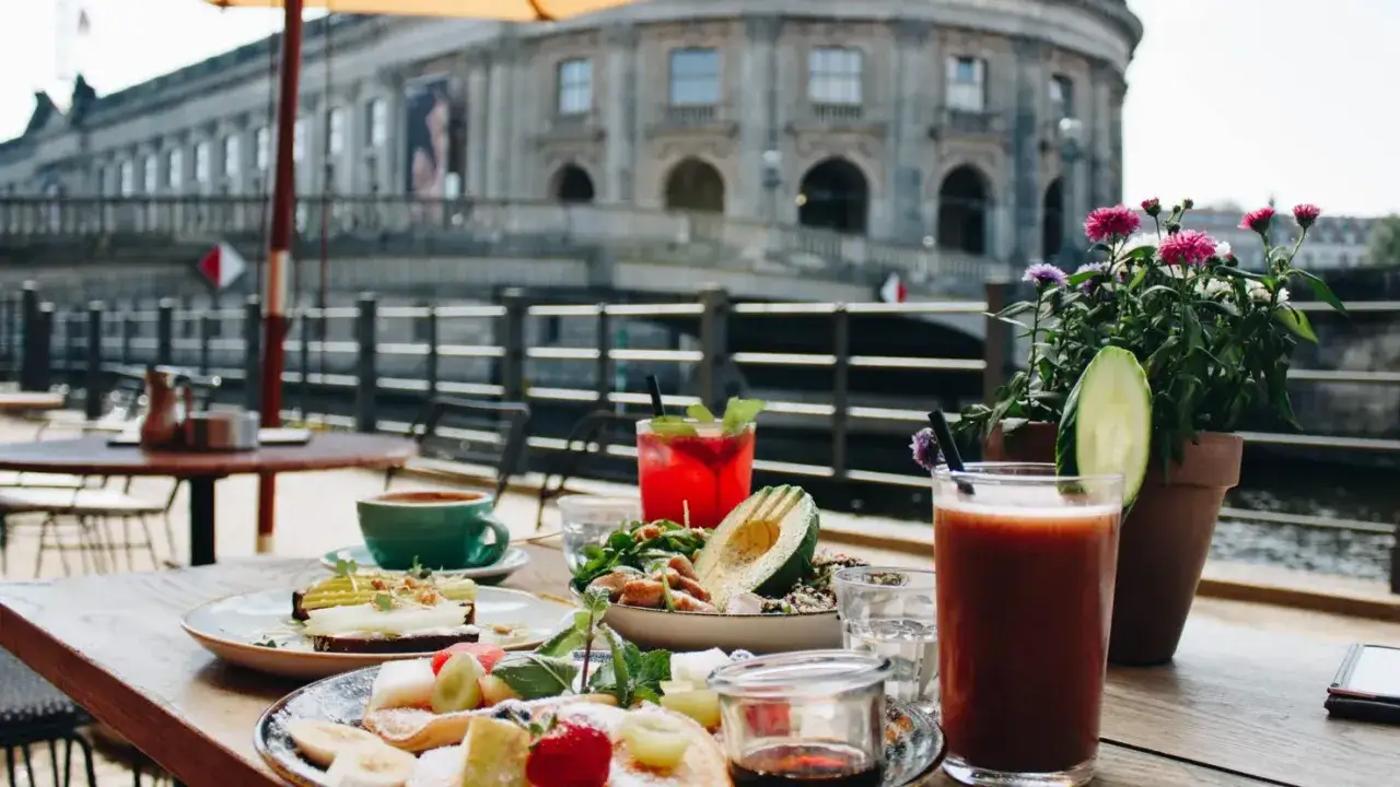 Leckeres Fr&uuml;hst&uuml;ck mit Fr&uuml;chten, Avocado und Kaffee auf einer Terrasse mit Blick auf ein historisches Geb&auml;ude in einem Caf&eacute; in Berlin Mitte.