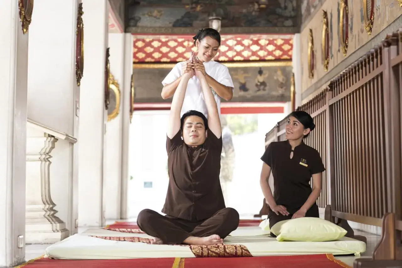 A man receives a traditional Thai massage, a practice with a rich history, from a therapist in a serene, temple-like setting.