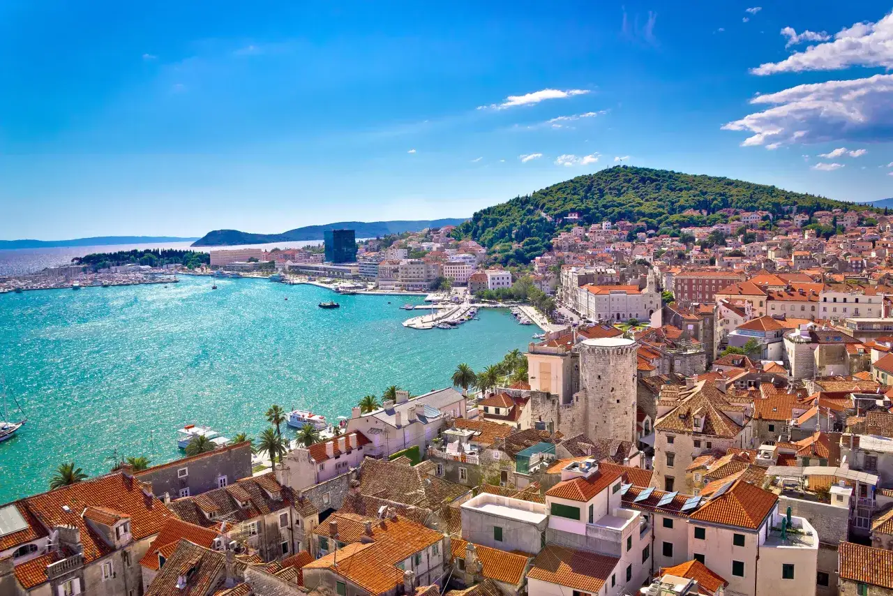 Widok na Split, perłę Dalmacji, gdzie leży, z turkusowym morzem i zielonym wzg&oacute;rzem w tle.