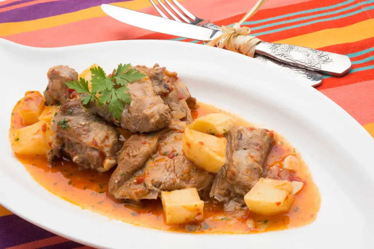 Sabroso cordero al chilindrón con patatas, servido en plato blanco sobre mantel colorido.