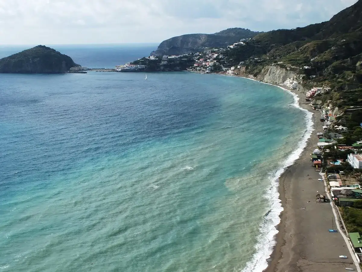 Vista aerea della spiaggia dei pescatori a Ischia, con case colorate aggrappate alla costa e acque turchesi.
