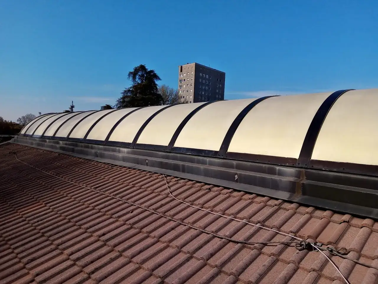 Tetto con tegole rosse e copertura curva in pannelli chiari, forse vernici termoriflettenti opinioni positive per l'efficienza energetica.
