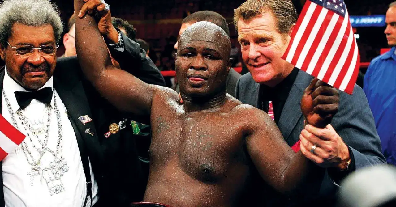 Boxer James Toney, with his arm raised, celebrates a victory. Don King and another man, holding an American flag, stand beside him.