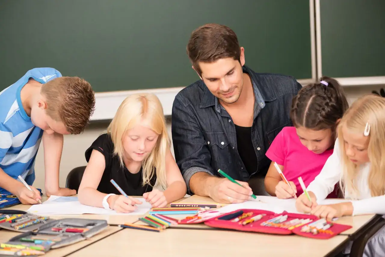 Ein Mann gibt Nachhilfe Realschule. Kinder konzentriert malen und schreiben an einem Tisch.