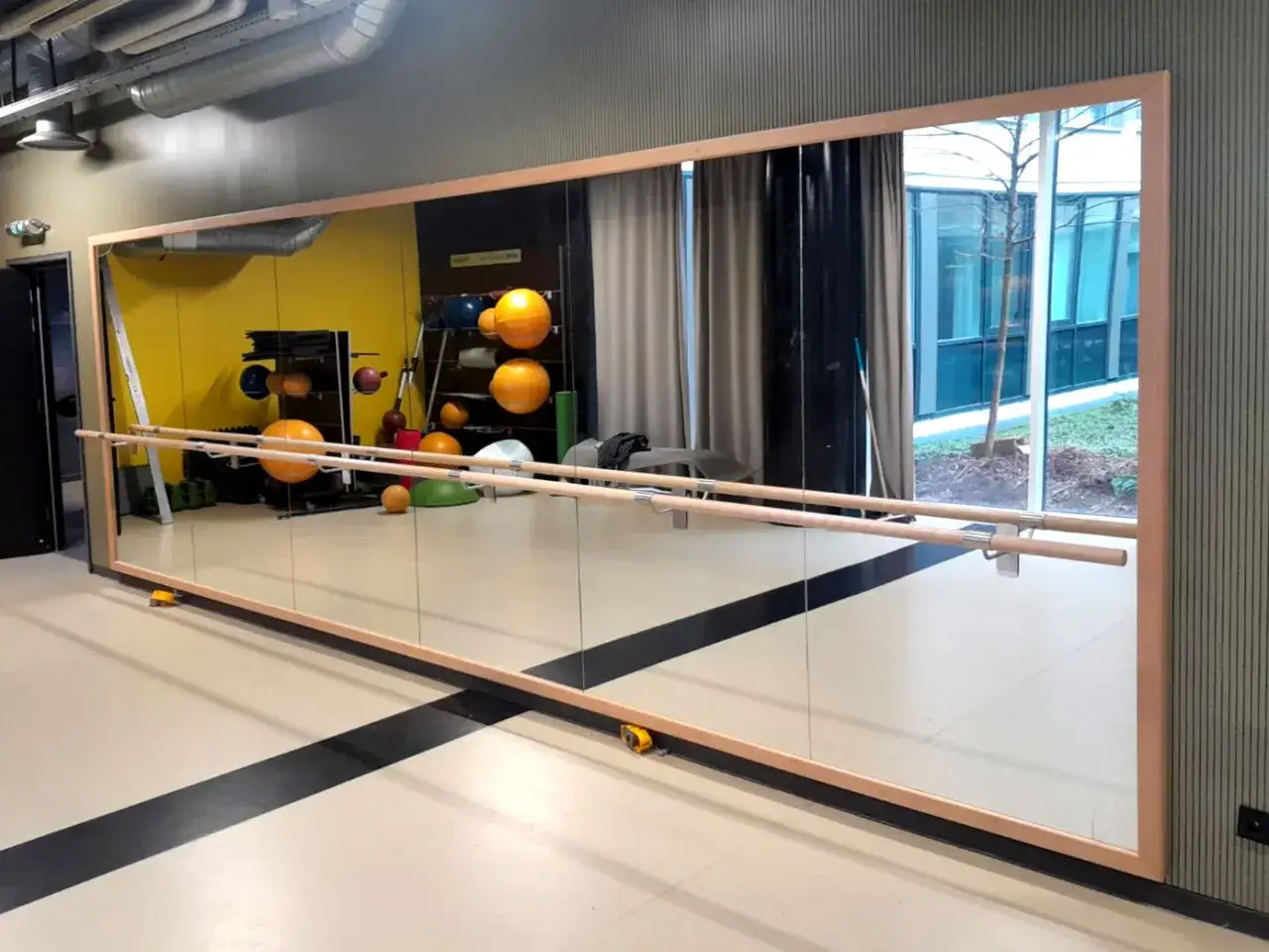 Sala luminosa con specchio a tutta parete, sbarre per balletto e attrezzature sportive, ideale per corsi di ballo e fitness.