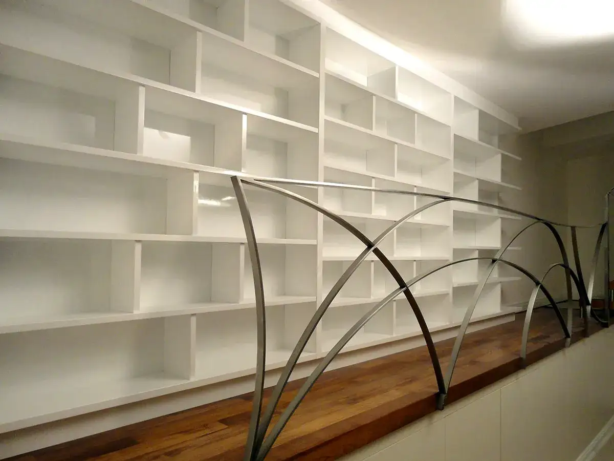 Ampia libreria in mansarda, con scaffali bianchi e un moderno corrimano in metallo curvo.