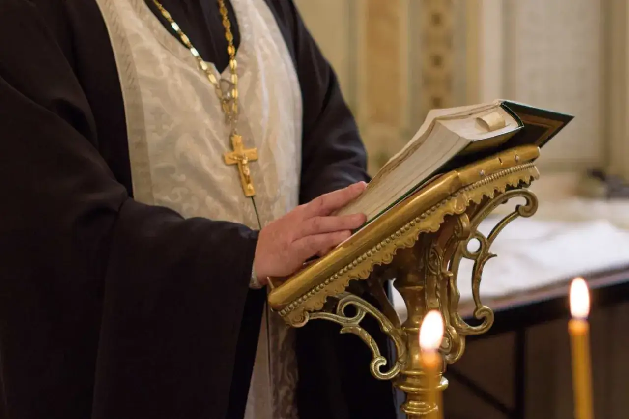 Duchowny w szatach z krzyżem na szyi czyta księgę na ozdobnym stojaku. Różnica między kościołem katolickim a prawosławnym w liturgii bywa subtelna.