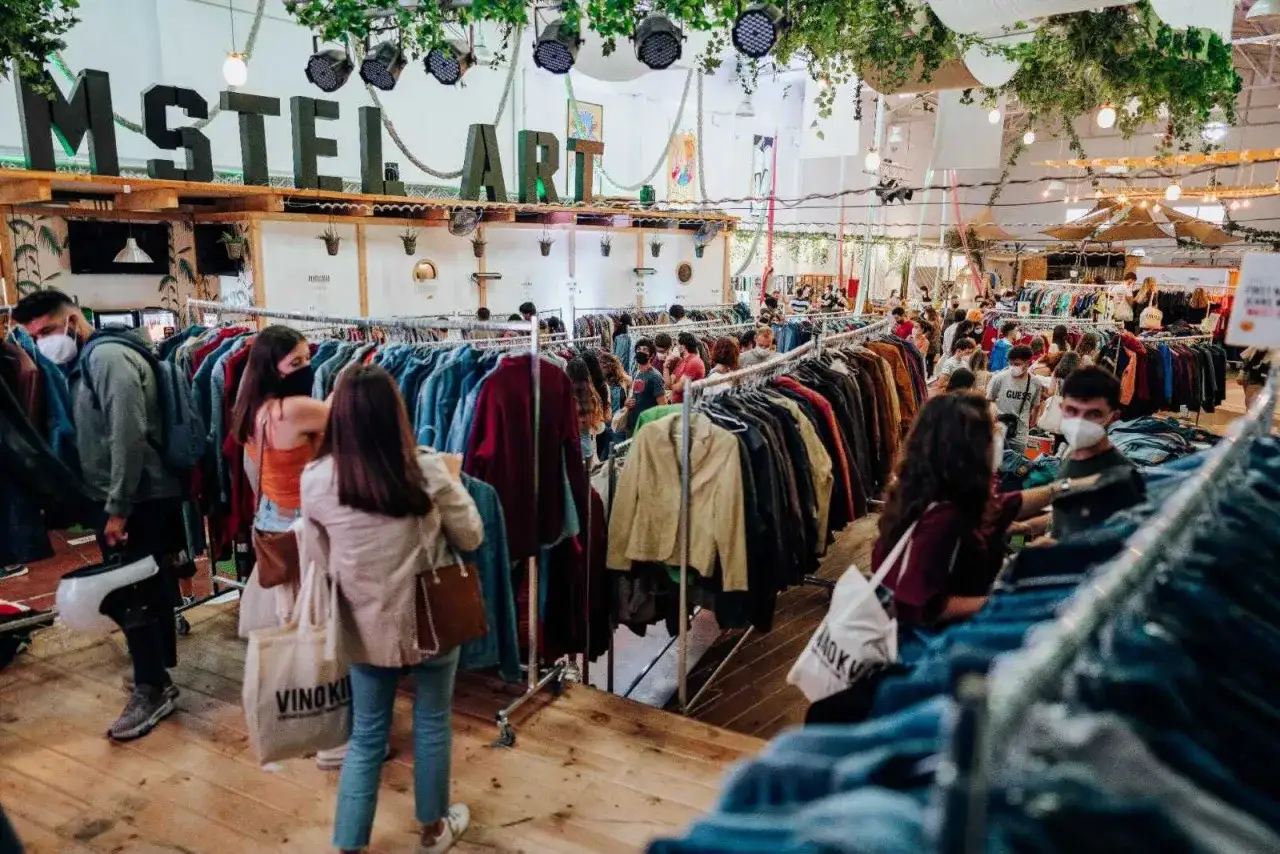 Gente buscando tesoros en un mercadillo vintage en Zaragoza. Ropa colgada en percheros, ambiente animado.