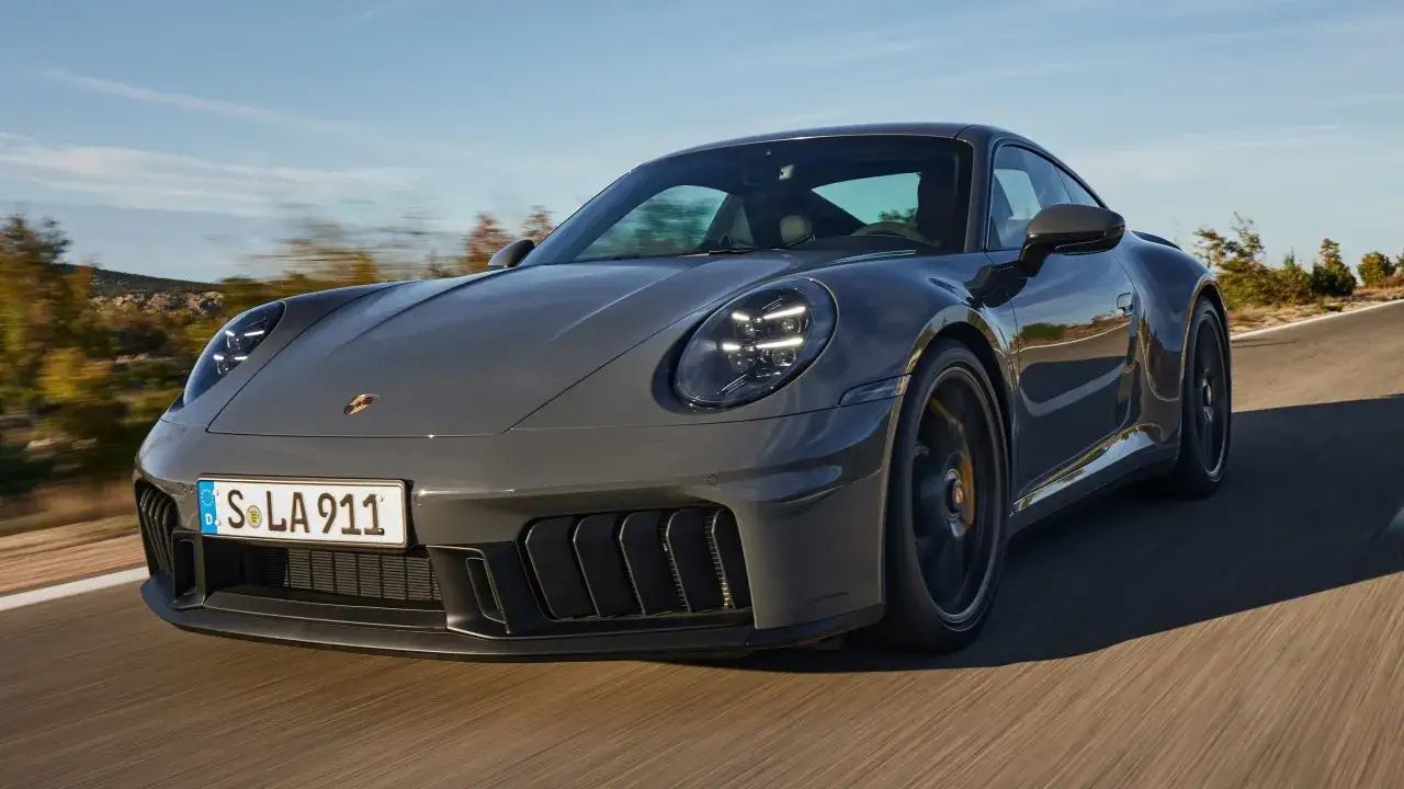 Szary Porsche 911 GTS pędzi po krętej drodze, otoczony jesiennym krajobrazem.
