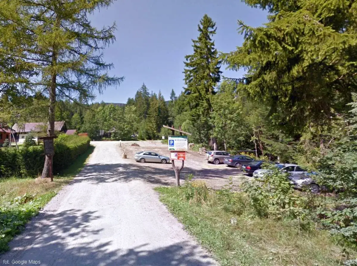 Droga do Babiej Góry prowadzi przez parking. Kilka samochodów czeka na turystów, gotowych do podjęcia wyzwania.